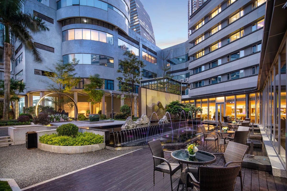 A modern hotel courtyard with a central water feature, outdoor seating, and a view of the building's exterior.