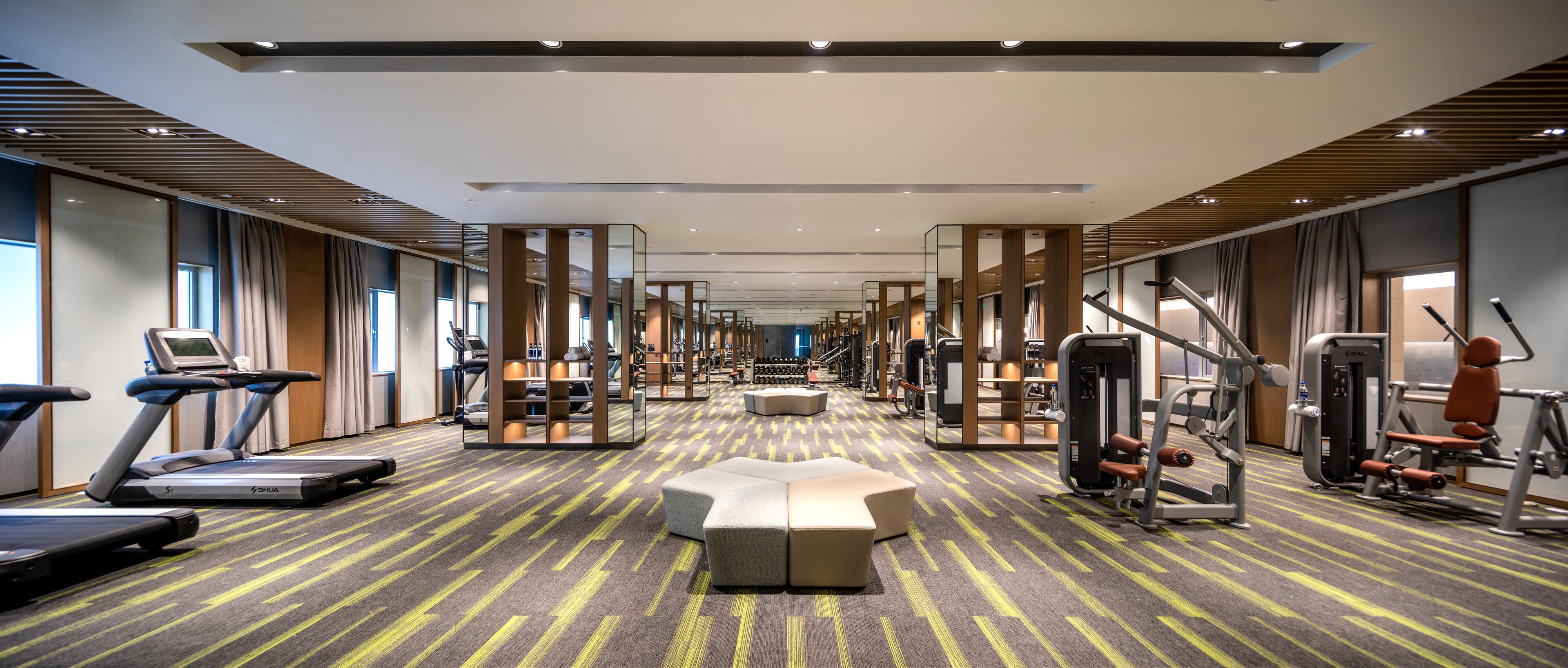 Une salle de sport moderne, équipée de tapis de course, d’appareils de musculation et d’un espace de repos central.
