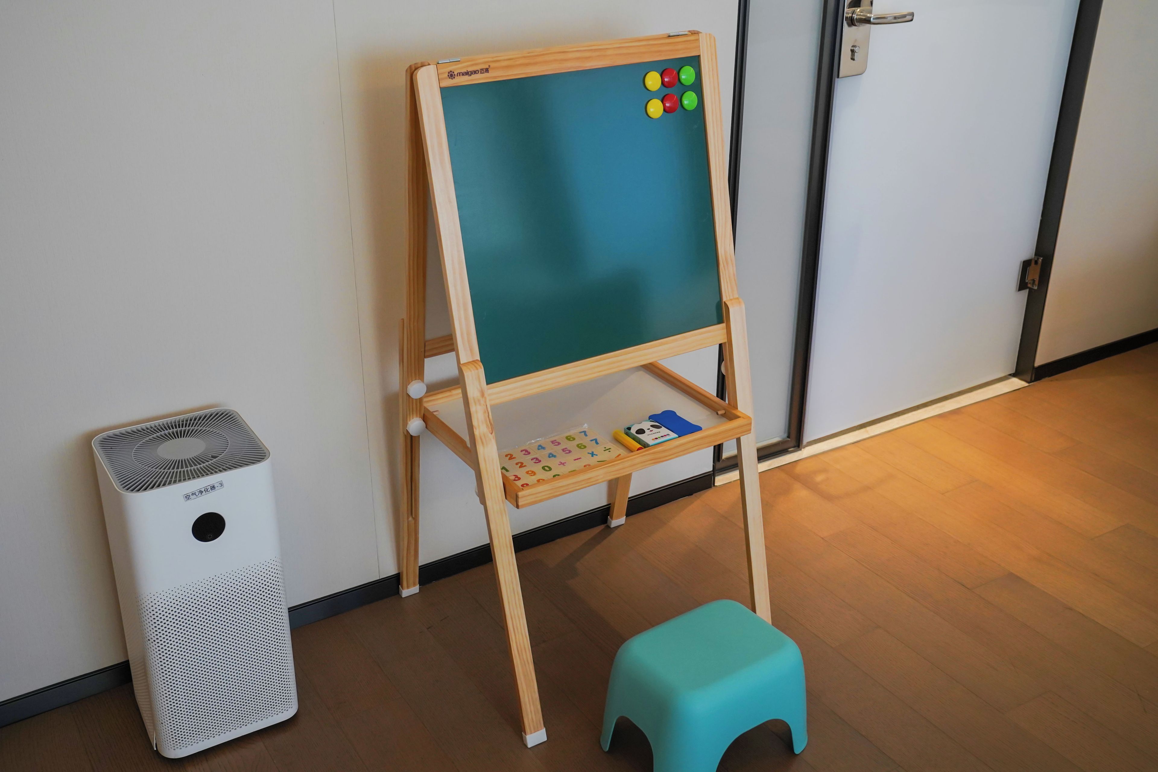 Une pièce comprenant un chevalet en bois, un petit tabouret, un purificateur d’air blanc et une porte.