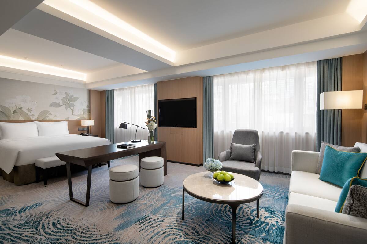 Ein modernes Hotelzimmer mit einem großen Bett, einem Schreibtisch, einer Sitzecke und einem Fernseher.