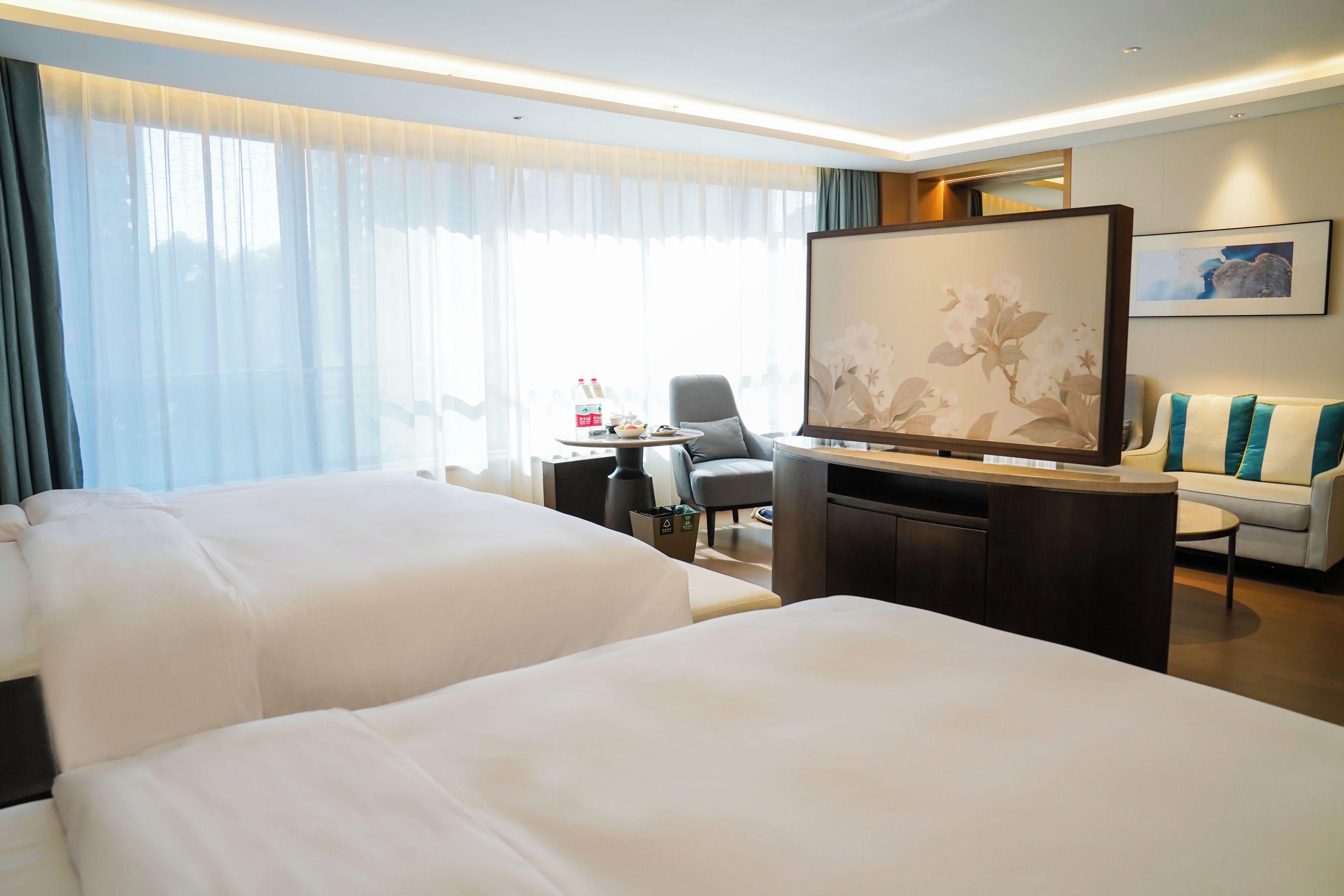 A hotel room with two beds, a desk, a chair, a sofa, and a large painting on the wall.