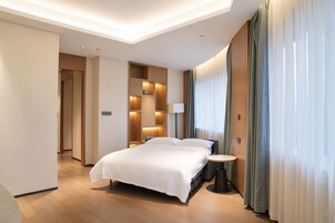 Una habitación de hotel moderna con una cama grande, mesitas de noche, una lámpara y vistas al exterior.