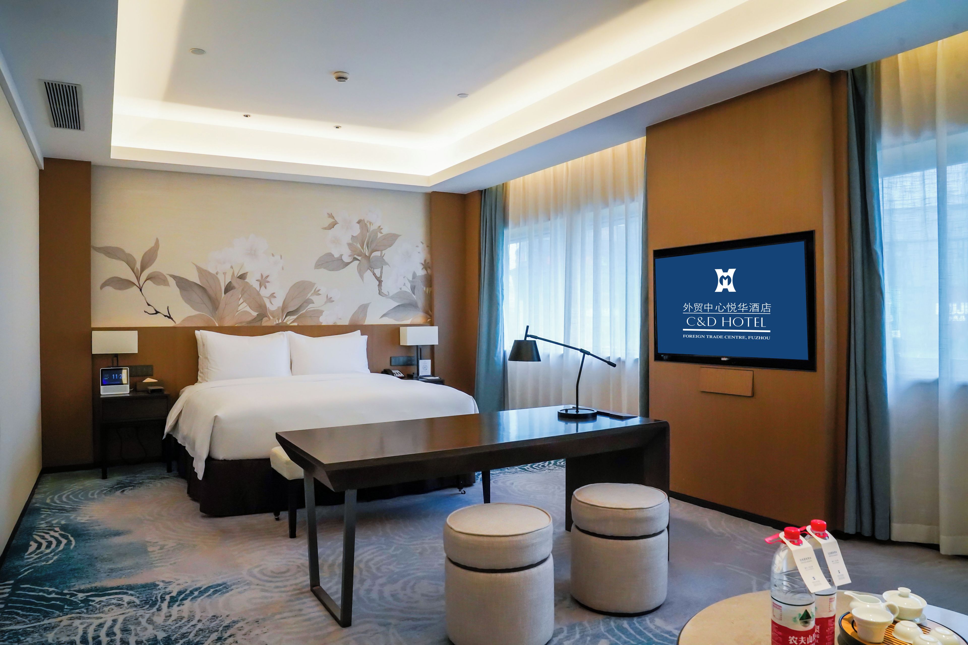 Une chambre d’hôtel équipée d’un lit, d’une table de chevet, d’une lampe, d’une télévision et d’un écran mural affichant des informations sur l’hôtel.