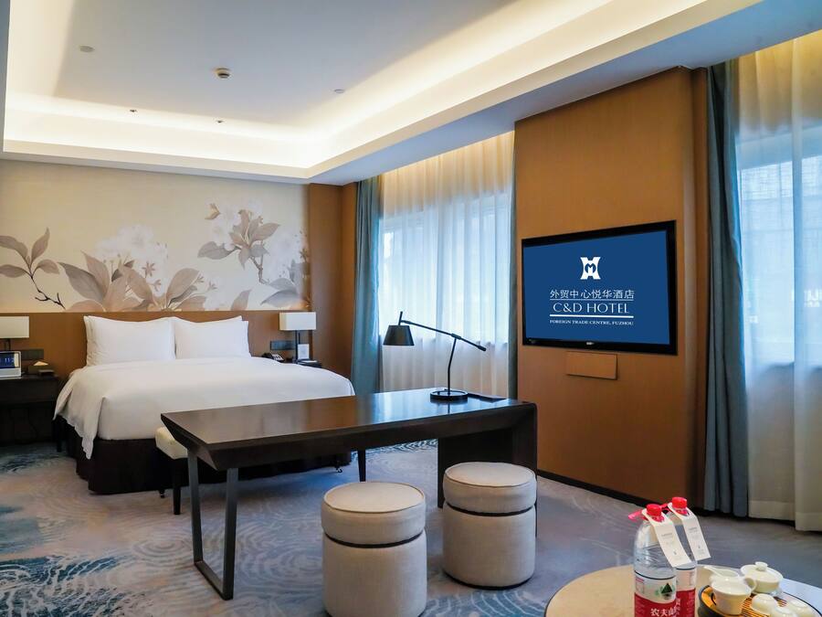 Une chambre d’hôtel équipée d’un lit, d’une table de chevet, d’une lampe, d’une télévision et d’un écran mural affichant des informations sur l’hôtel.