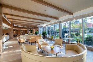 Un hall d’entrée spacieux, doté de meubles modernes, de grandes fenêtres et offrant une vue sur l’extérieur.
