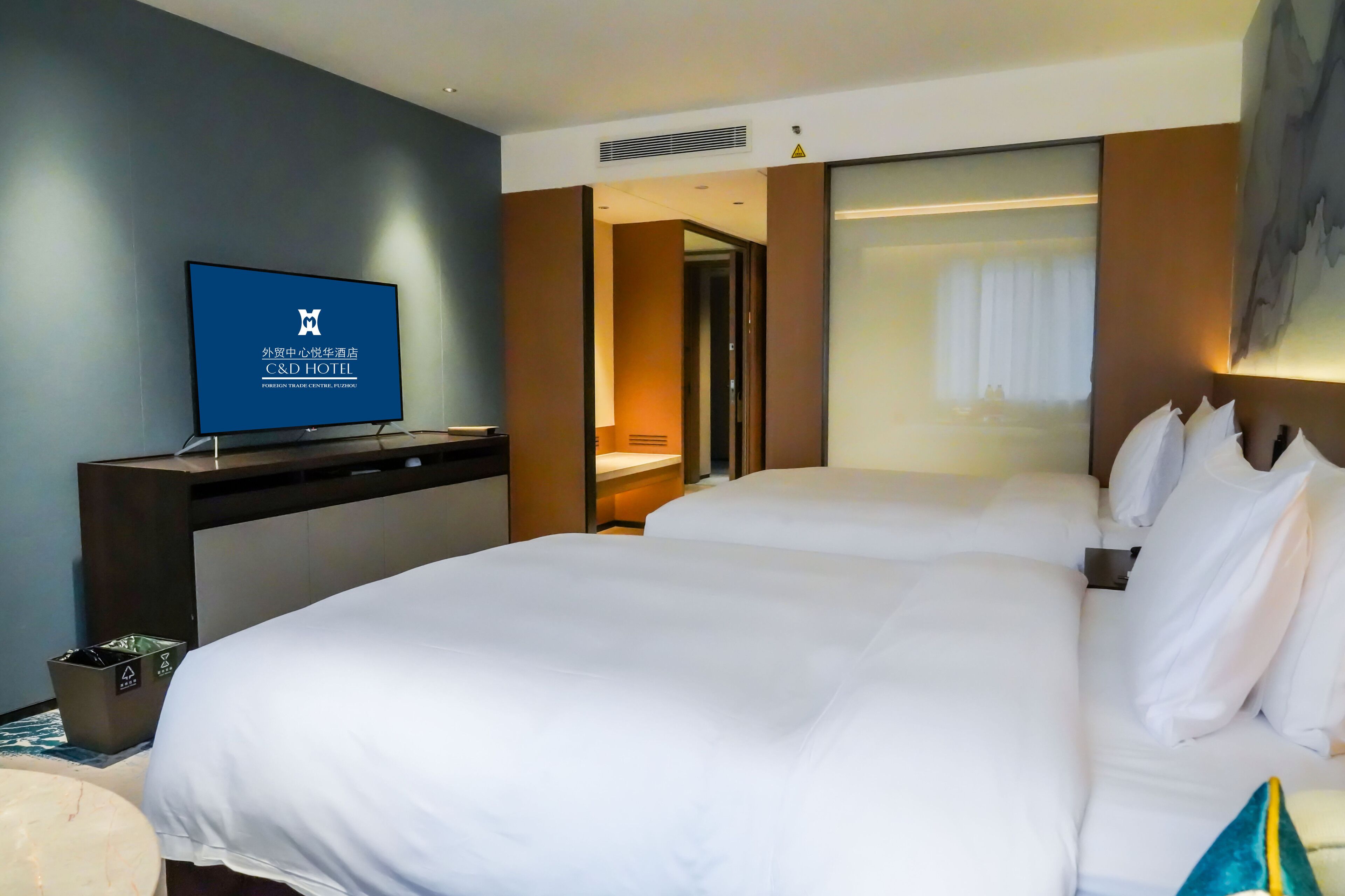 Habitación de hotel con una cama grande, un televisor sobre un mueble y vista al pasillo.