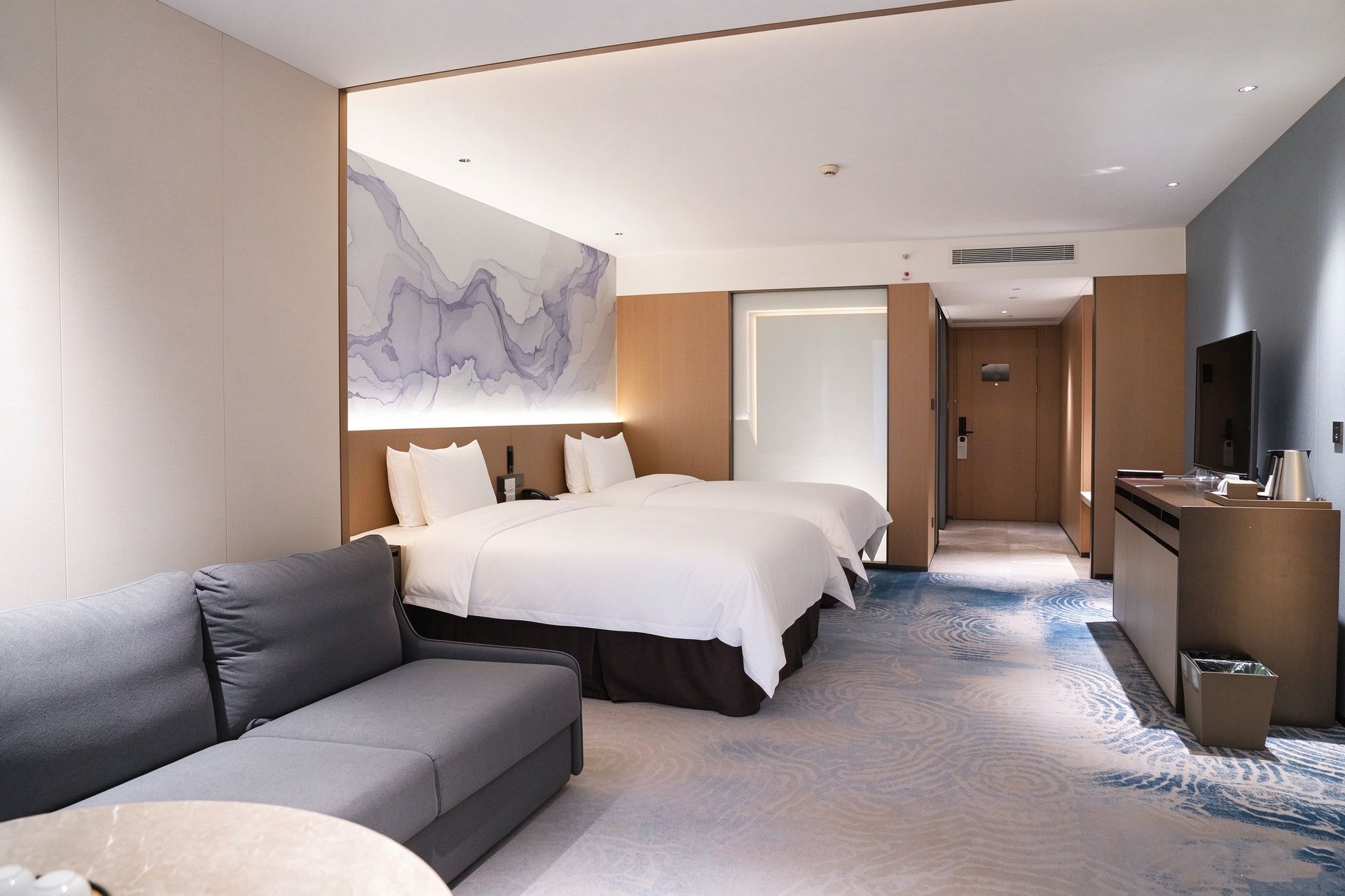Une chambre d’hôtel avec un grand lit, un canapé, un bureau avec une télévision et une salle de bain visible à travers une porte ouverte.
