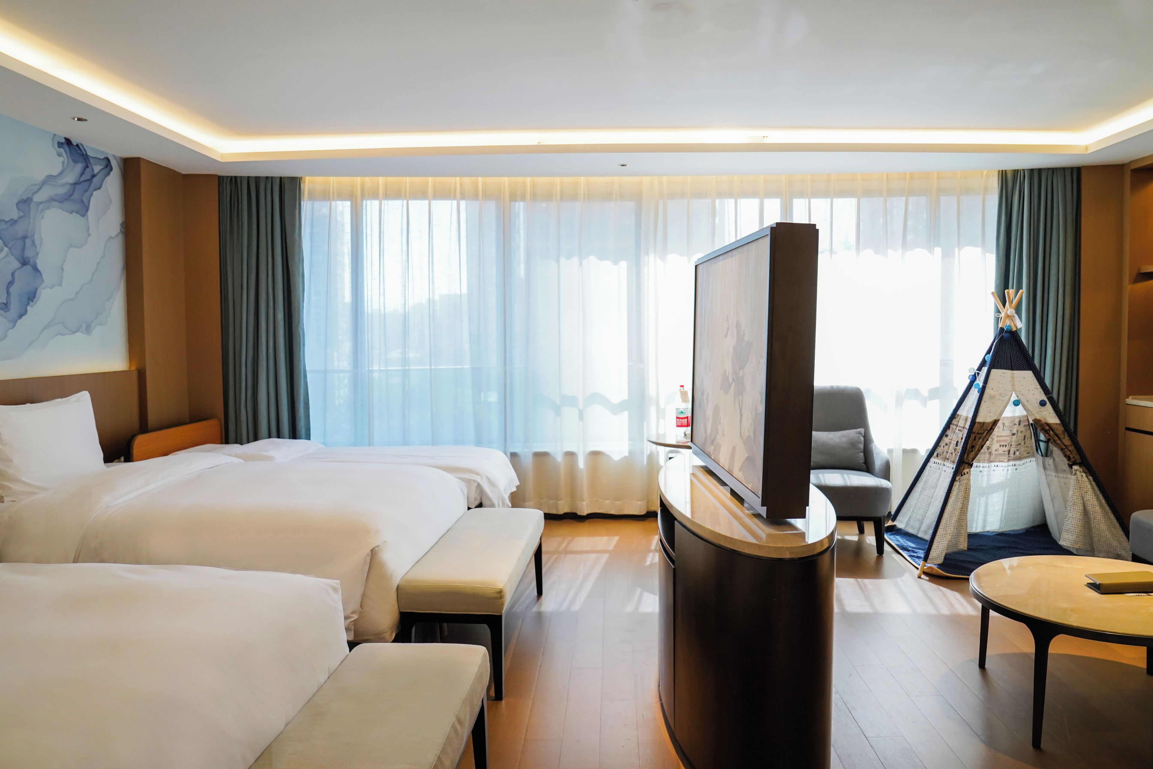 Een hotelkamer met twee bedden, een flatscreen-tv, een klein tafeltje en een decoratief tipitentje.