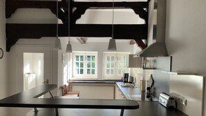 Una cocina moderna con una isla central, luces colgantes y ventanas amplias.