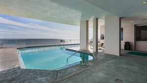 Un área de piscina con vista al océano, una zona de estar con mesas y sillas, y una sección cubierta con vista al mar.