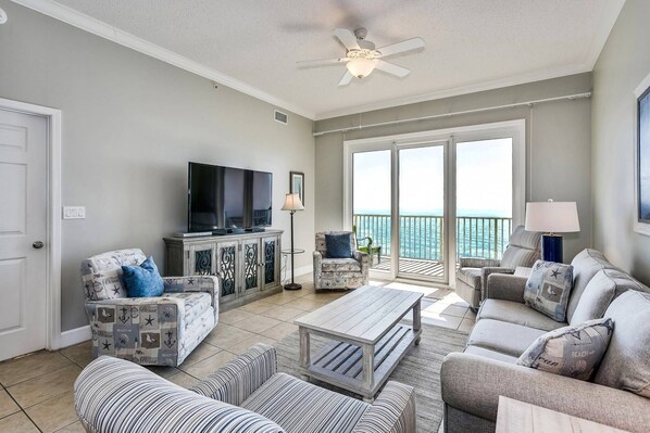 A spacious living room with a television, comfortable seating, and a balcony with a view.