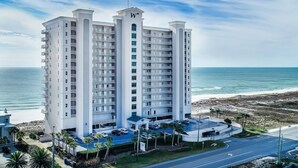 Un hotel moderno con varios balcones, un estacionamiento y vista a la playa.