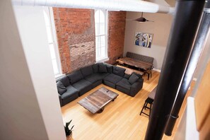 A loft-style living room with exposed brick walls, a sectional sofa, a wooden coffee table, and a dining area.