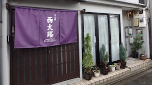 A building with a purple banner reading "Guest House Nishioji" and a brown gate. There are potted plants on the sidewalk.