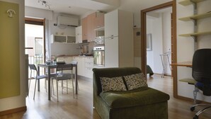Ein gemütlicher Wohnbereich mit Küchenzeile, Essplatz und einem grünen Sofa mit gemusterten Kissen.