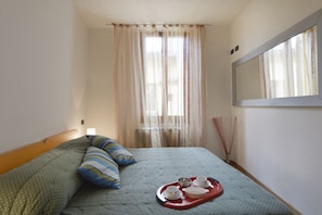 A neatly made bed with a tray of breakfast items, a large mirror, and sheer curtains.