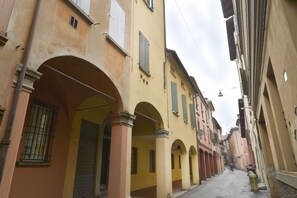 A narrow street with buildings featuring arched doorways and balconies. - UR-NEST Sant' Apollonia (Bologna)