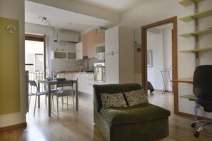 A compact living space with a kitchenette, a dining area, and a green sofa with patterned cushions. - UR-NEST Sant' Apollonia (Bologna)