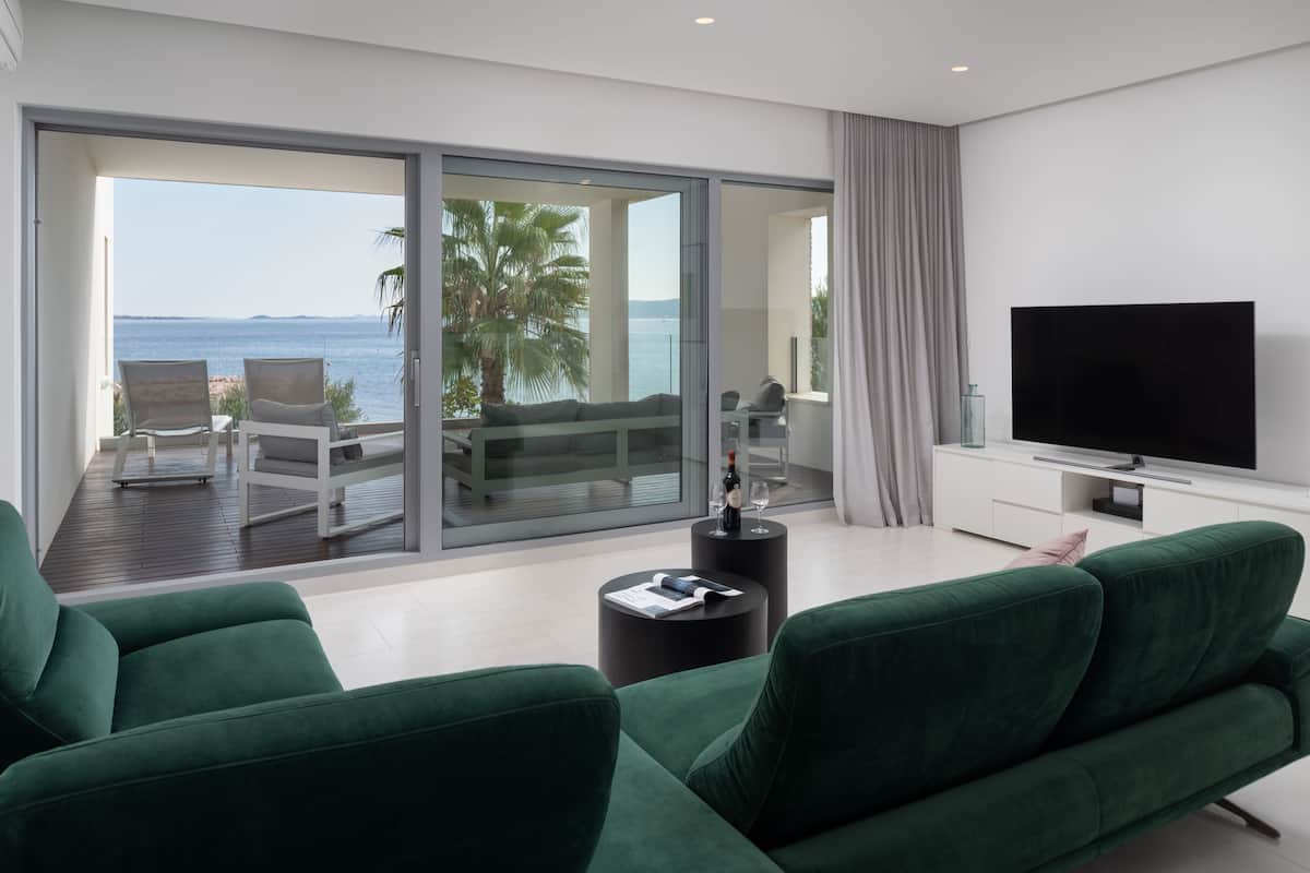 Una sala de estar moderna con sofás verdes, un televisor de pantalla plana y un balcón con vista al mar.