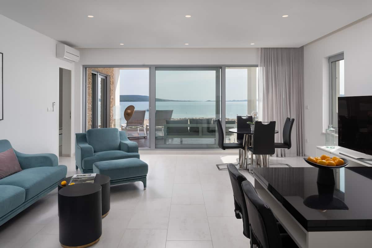 Una sala de estar moderna con un sofá, sillones, un comedor y vista al mar.