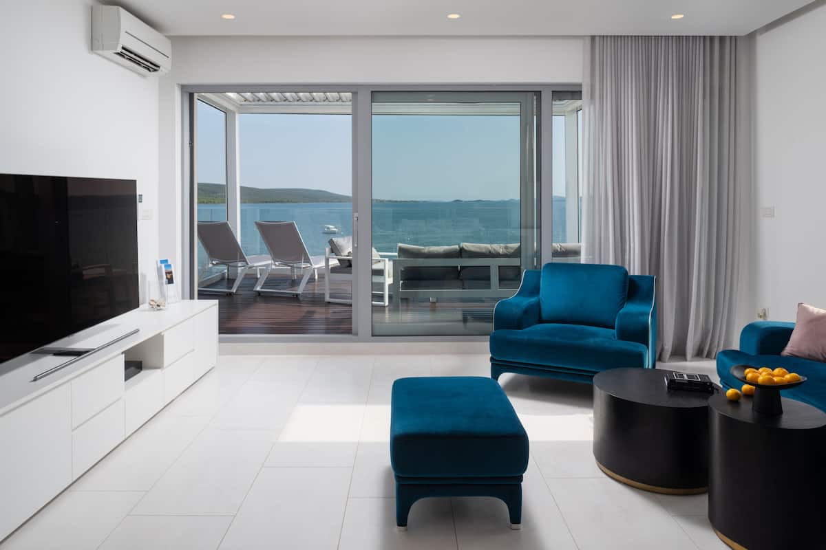 Una sala de estar moderna con televisor, un sofá azul, una mesa redonda para café y un balcón con vista al mar.