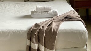 Ein ordentlich bezogenes Bett mit weißen Leinen, einer gemusterten Tagesdecke und einem gefalteten Handtuch.