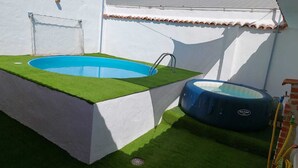 Una piscina pequeña al aire libre con césped artificial y un jacuzzi.