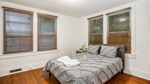 Ein Schlafzimmer mit einem Bett, Holzjalousien, einem Nachttisch und einer Lampe.
