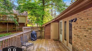 Eine Holzterrasse mit überdachter Sitzgruppe, einer Ziegelwand und einer Tür zu einer überdachten Veranda.