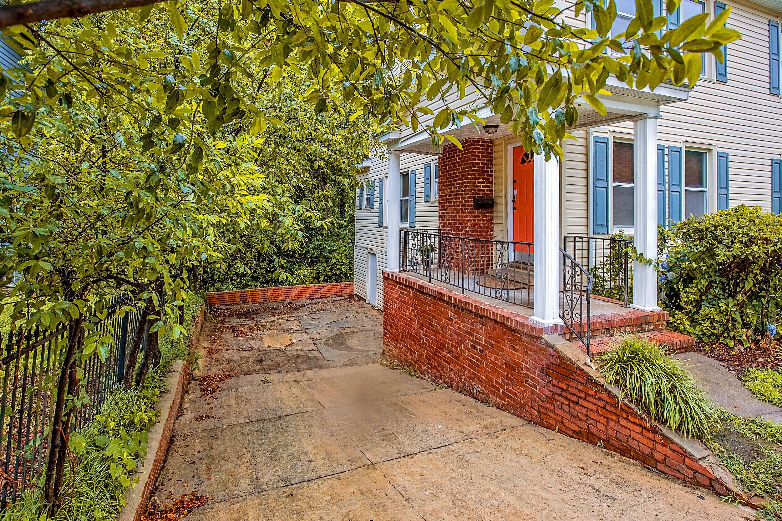 A two-story house with a brick entrance, a porch with a railing, and a garden area with a fence and greenery.
