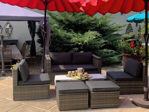 An outdoor seating area with wicker furniture, a table with decorative items, and a potted plant with red flowers.