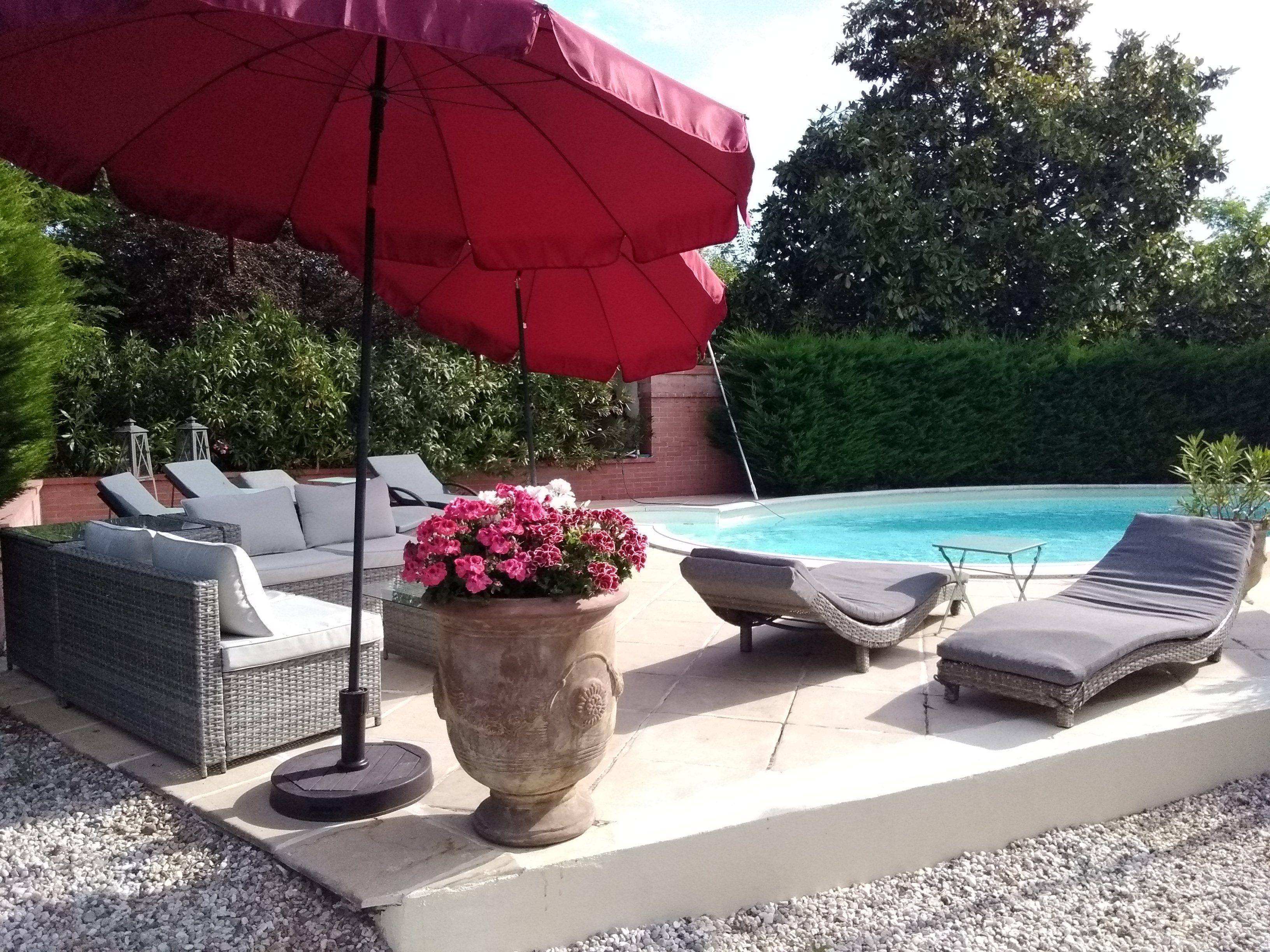 A poolside area with lounge chairs, a red umbrella, and a planter with flowers.