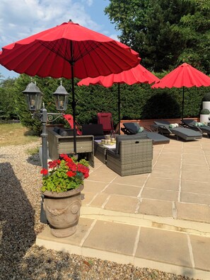 An outdoor patio with red umbrellas, wicker furniture, and a stone floor. - 19th-century building, 3 stars *** (Arsac)