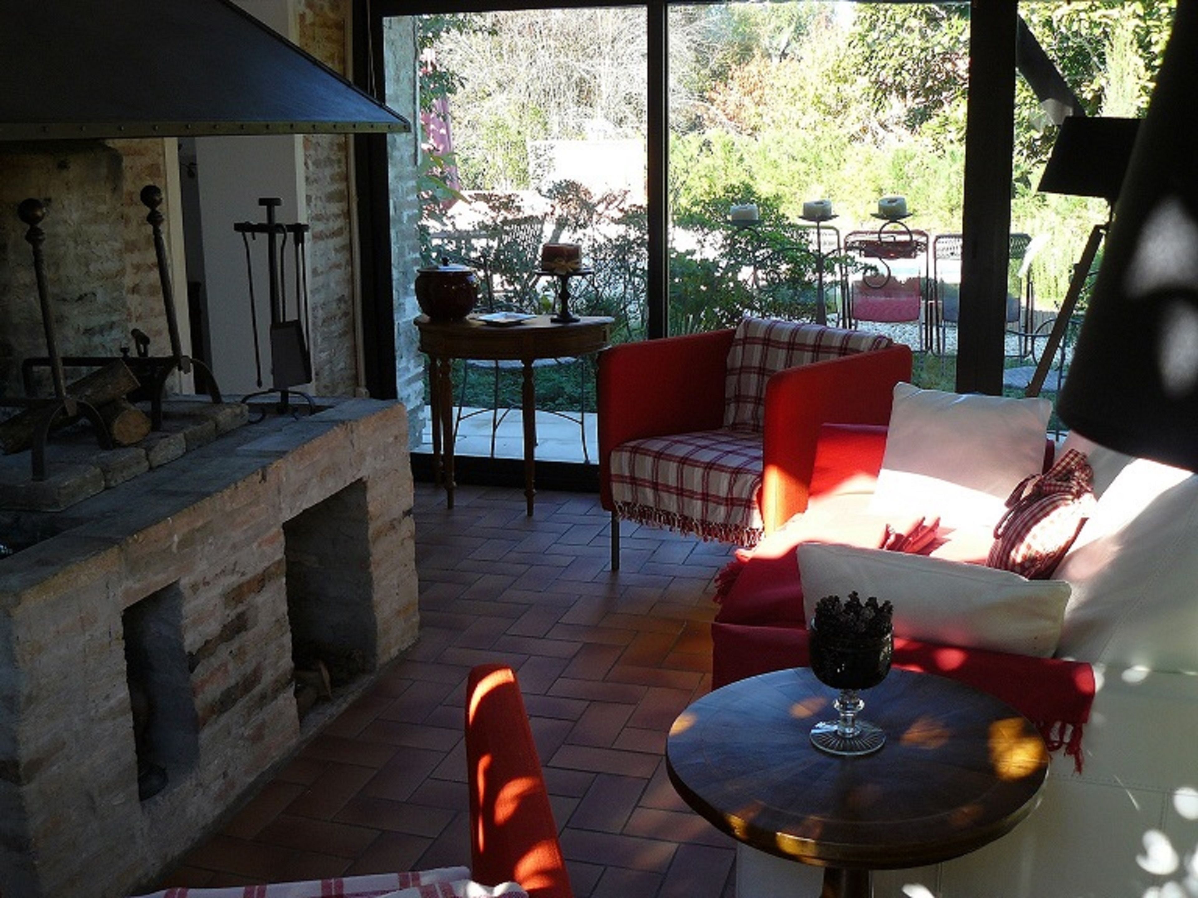 A cozy outdoor seating area with a fireplace, a table with a glass, and a view of greenery.