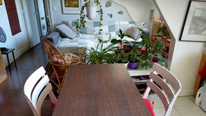 Una habitació acollidora amb taula de dinar de fusta, cadires de vimet, sofà amb coixins i diverses plantes en testos.