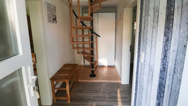 Una scala a chiocciola con gradini in legno e ringhiere nere, una panca di legno e una porta con un pannello in vetro sabbiato.