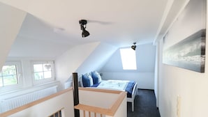 Una camera da letto con soffitto spiovente, un letto con lenzuola blu, una finestra e un quadro appeso al muro.