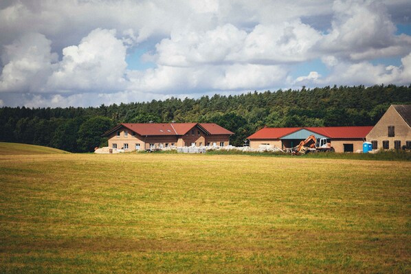A rural landscape with two buildings, one under construction, and a field in the foreground.