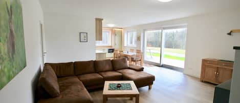 A living room with a brown sectional sofa, a wooden coffee table, and a kitchen area in the background.