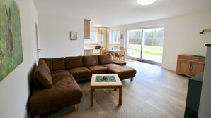 Un salon avec un canapé d’angle marron, une table basse en bois et, au fond, un espace cuisine.