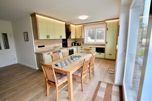 A modern kitchen with wooden cabinets, a dining table with chairs, and a large window providing natural light.
