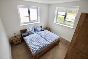 A bedroom with a wooden bed, two bedside tables, and two windows with blinds.
