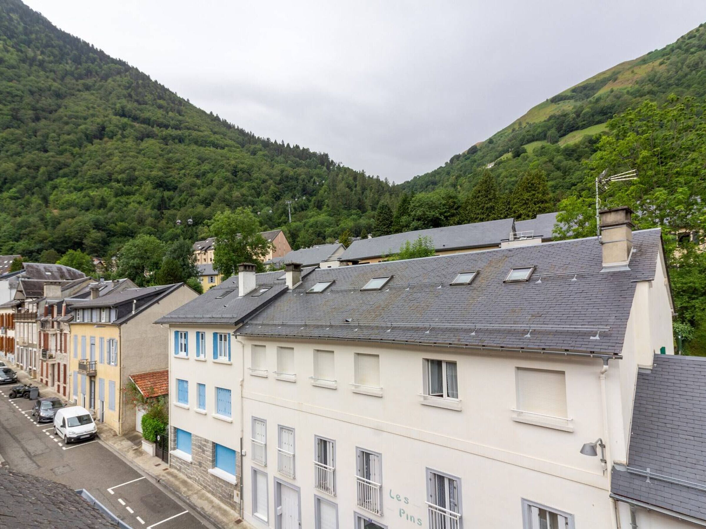 Vista de una calle con edificios, una carretera y una colina boscosa al fondo.