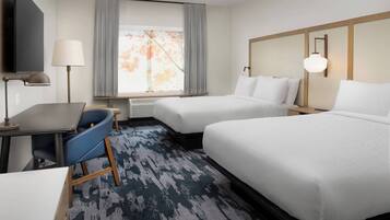 A hotel room with two beds, a desk, a chair, a TV, and a window with curtains.