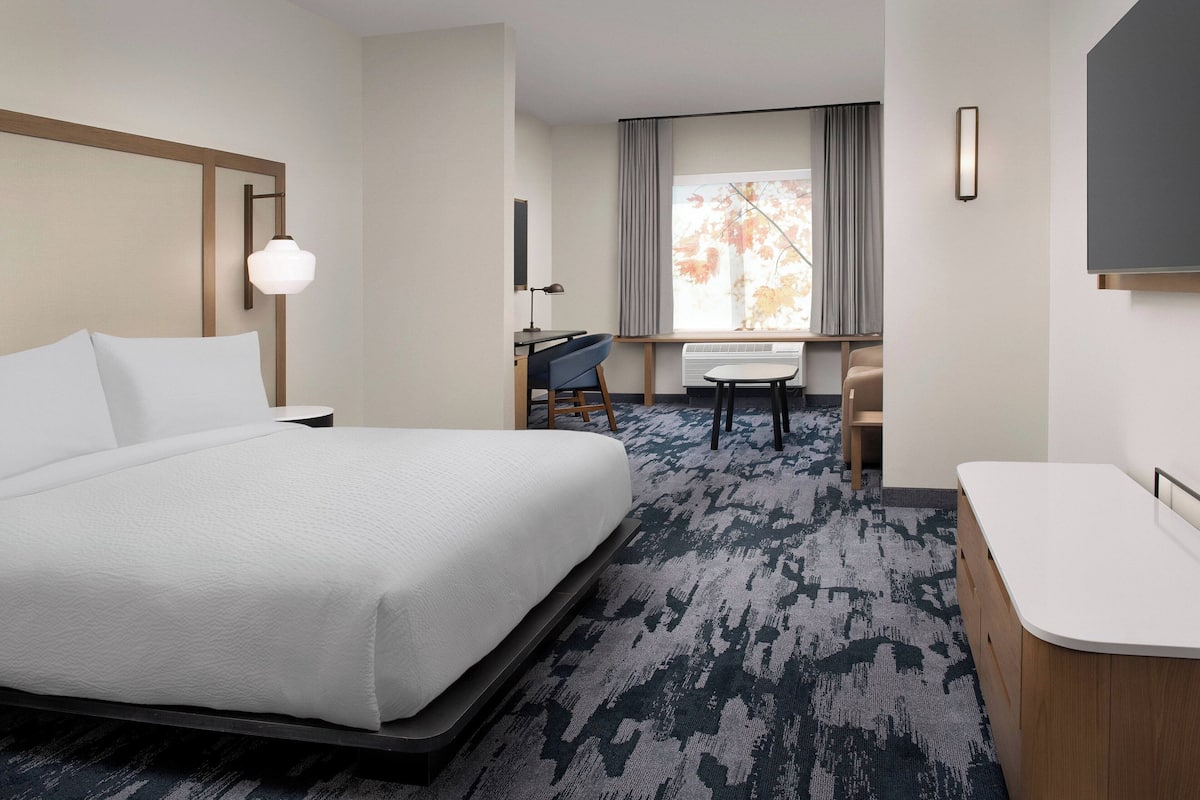 A hotel room with a large bed, a desk, a chair, a small table, and a TV.