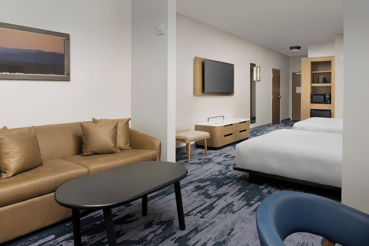 A hotel room with a sofa, a desk, a bed, a chair, and a TV mounted on the wall.