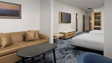 A hotel room with a sofa, a desk, a bed, a chair, and a TV mounted on the wall.
