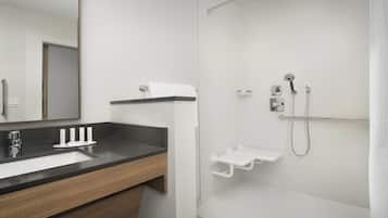 Un baño moderno con lavamanos de superficie negra, un espejo, ducha con cabezal de mano y un perchero blanco.