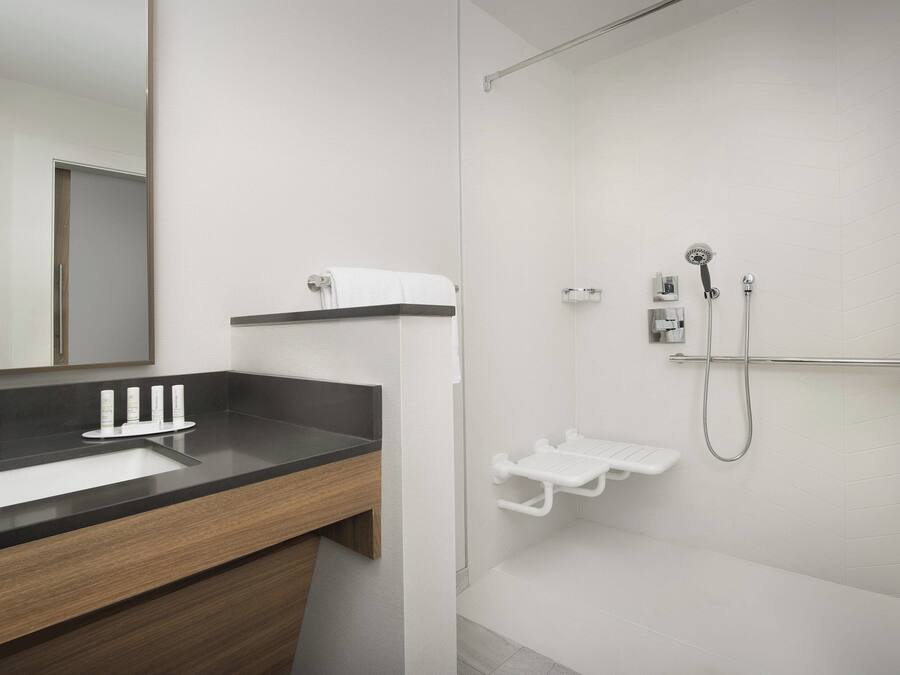 Un baño moderno con lavamanos de superficie negra, un espejo, ducha con cabezal de mano y un perchero blanco.