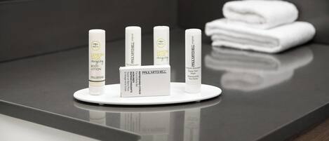 A bathroom counter with various Paul Mitchell products, including body lotion and shampoo, and a stack of white towels.